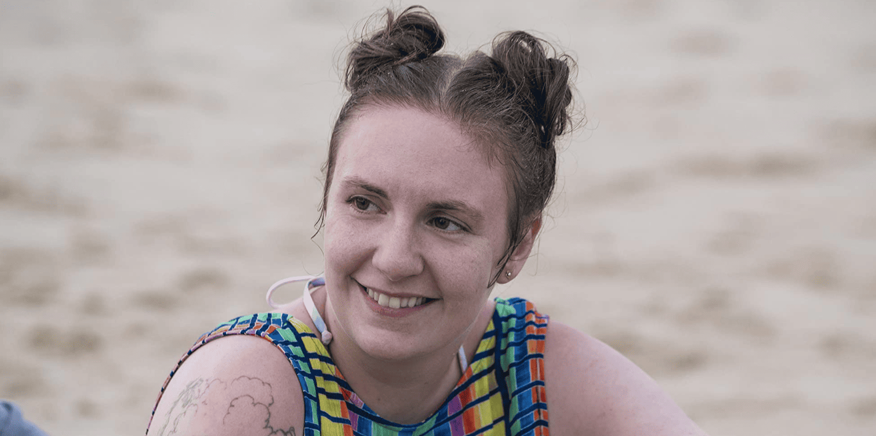 Hannah relaxing beachside while wearing two bun knots on top of her head in this image from Apatow Productions