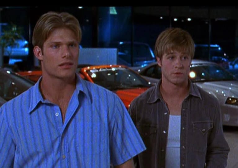 Two men stand in a parking lot in this image from Warner Bros. Studios.