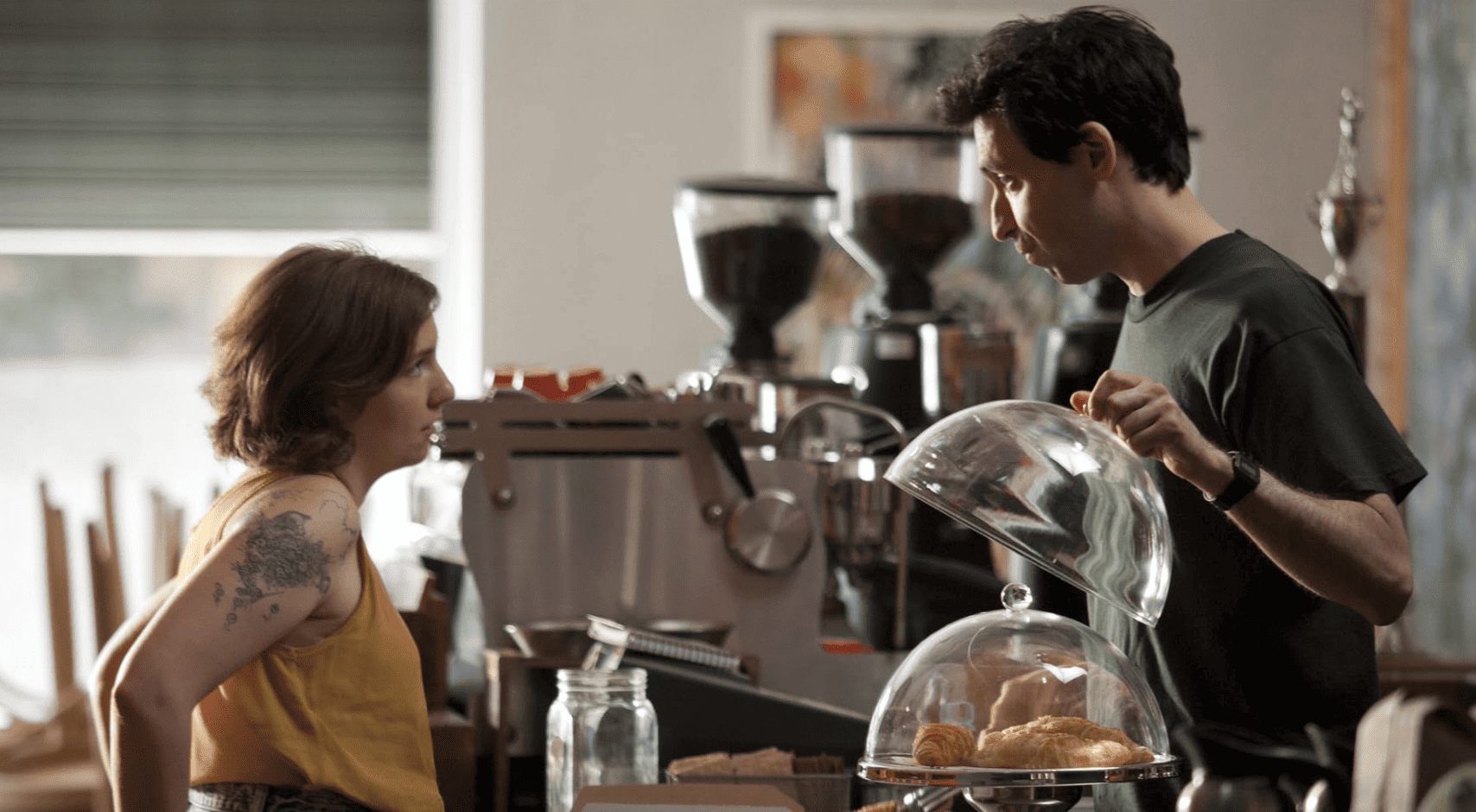 Hannah and Ray are standing opposite each other while working at his cafe and staring lovingly into each other’s eyes in this image from Apatow Productions