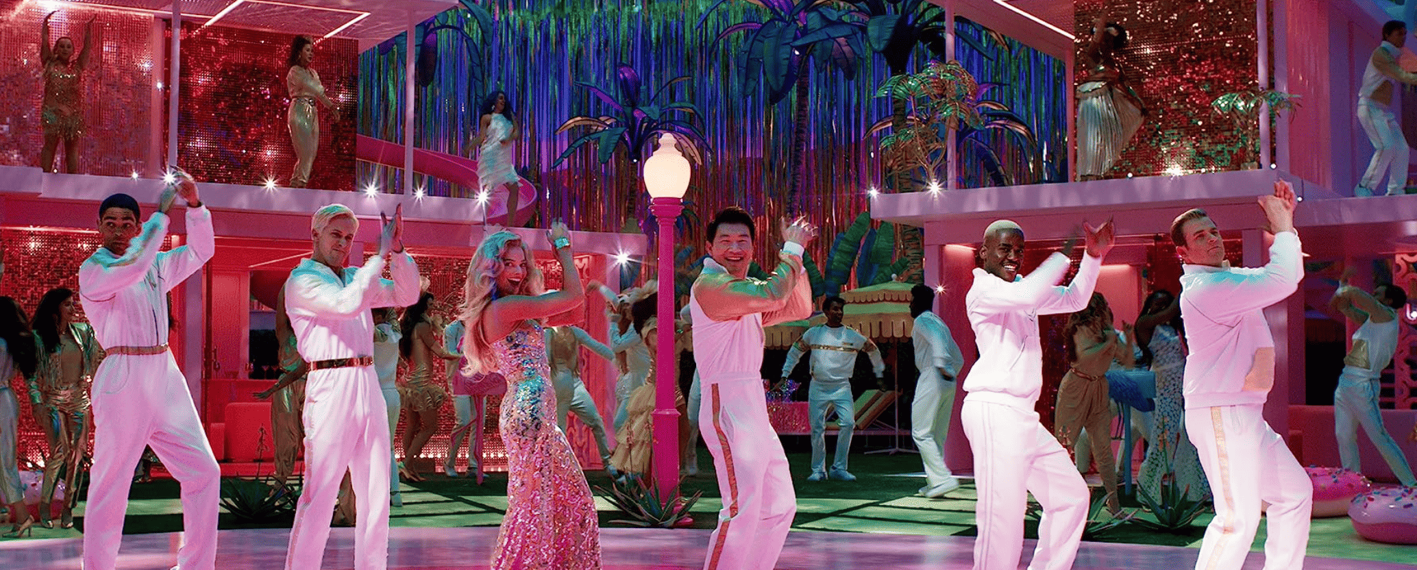 Margot Robbie as Barbie and Simu Liu as Ken wear disco-inspired outfits and dance on a crowded dance floor in this image from Warner Bros.