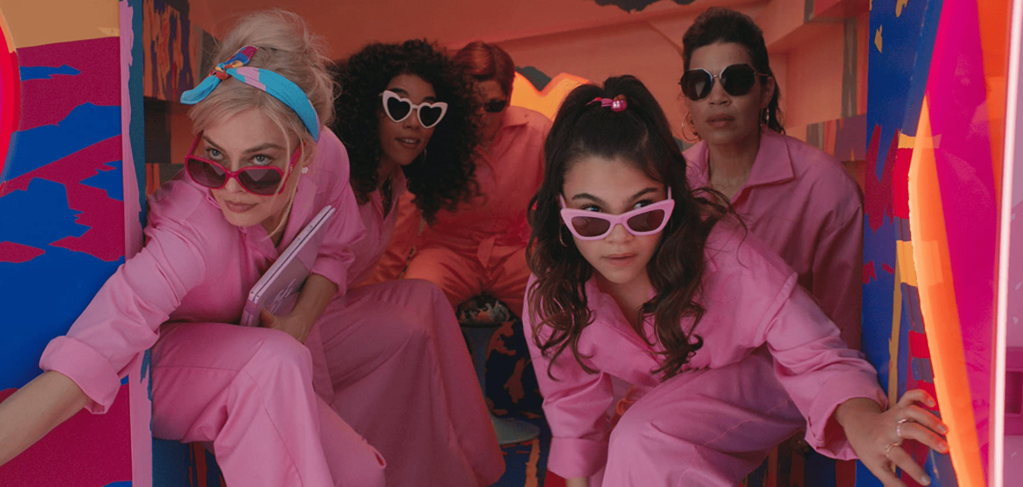 Margot Robbie, Alexandra Shipp, Michael Cera, America Ferrera, and Ariana Greenblatt climb out of the back of a truck wearing all-pink coveralls in this image from Warner Bros