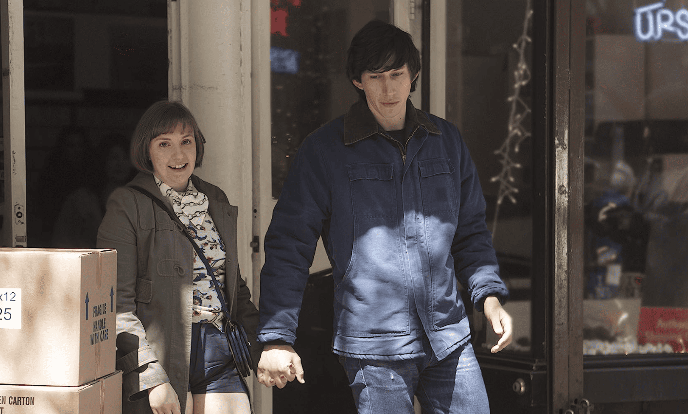 Adam Driver holding hands with Lena Dunham as they step out of a store in this image from Apatow Productions