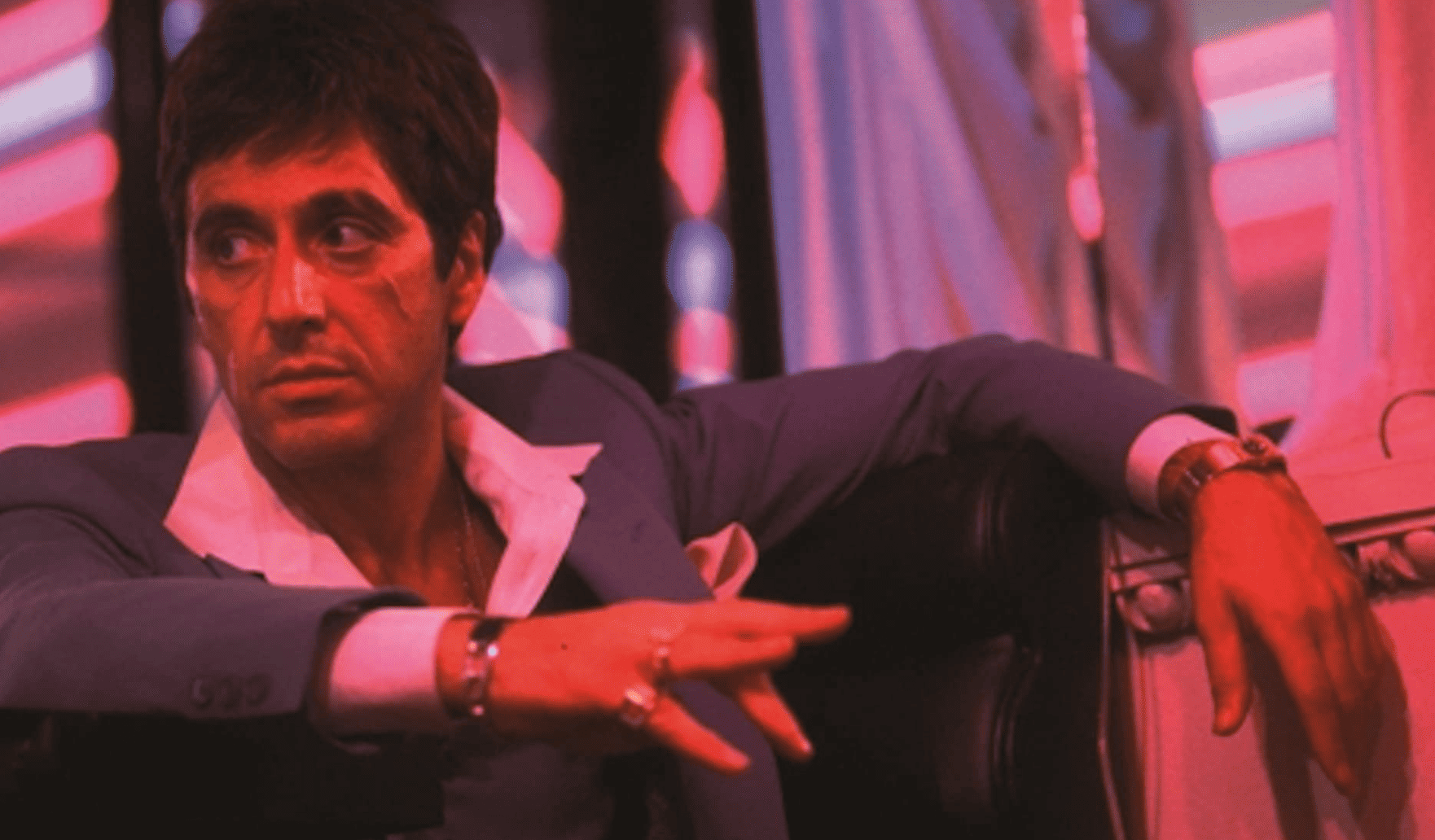 Al Pacino sitting at a club wearing heavy rings on his fingers and holding a cigar in this image from Universal Pictures