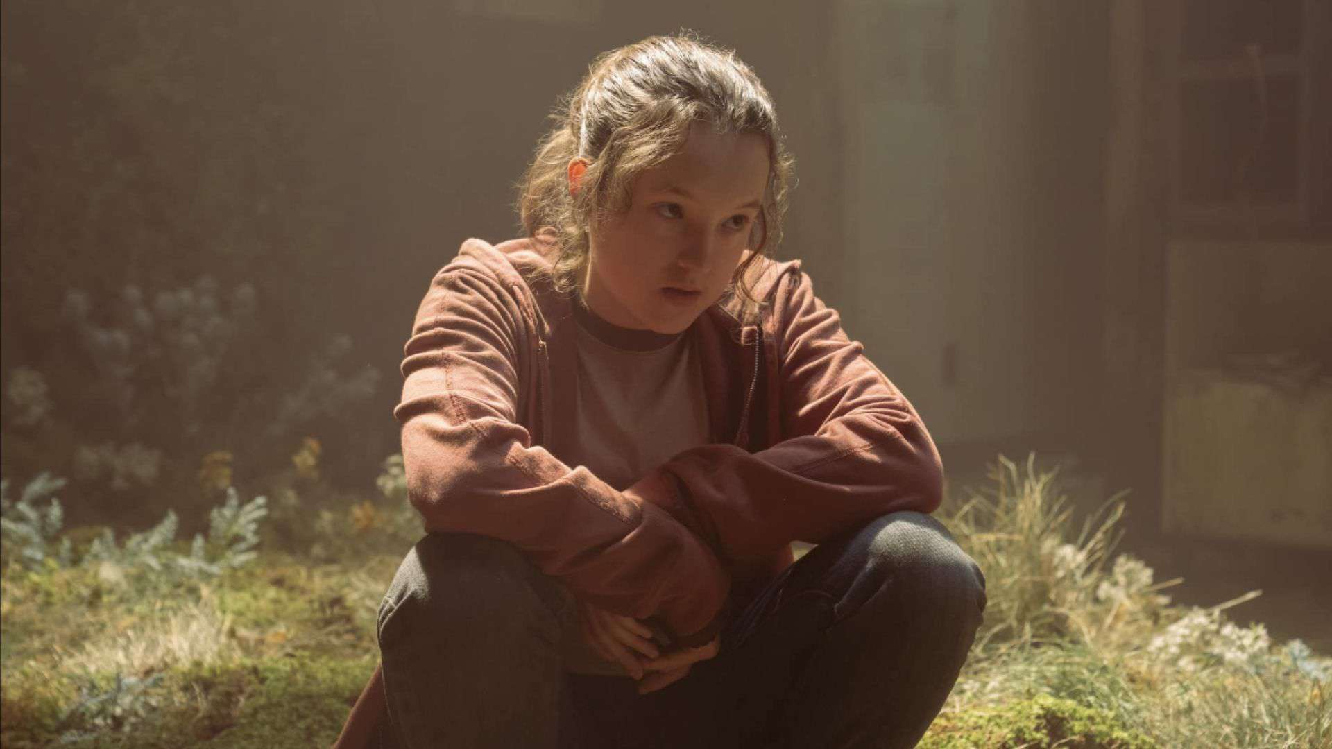 Bella Ramsey in a red sweater sitting on grass in this image from Sony Pictures Television.
