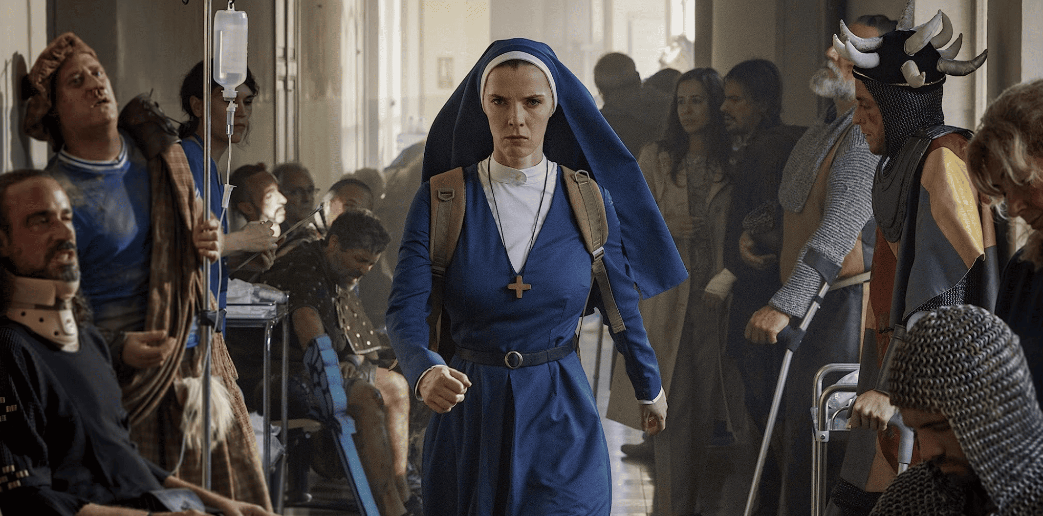 Betty Gilpin defiantly walks through a hospital full of odd-looking characters, including someone who appears to be a knight in this image from Warner Bros. Television.