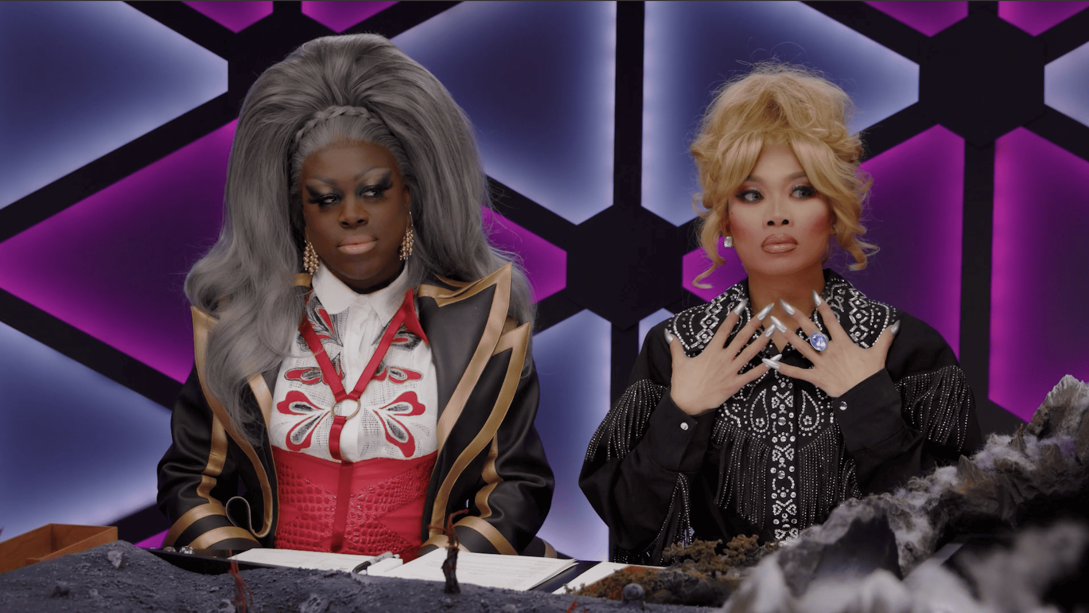 Two drag queens sit next to each other, one gasping, in a game of Dungeons and Dragons in this image from Dropout