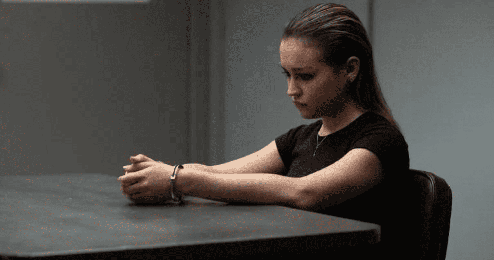 A teenage girl sits at a table handcuffed in a police station in this photo by Entertainment One