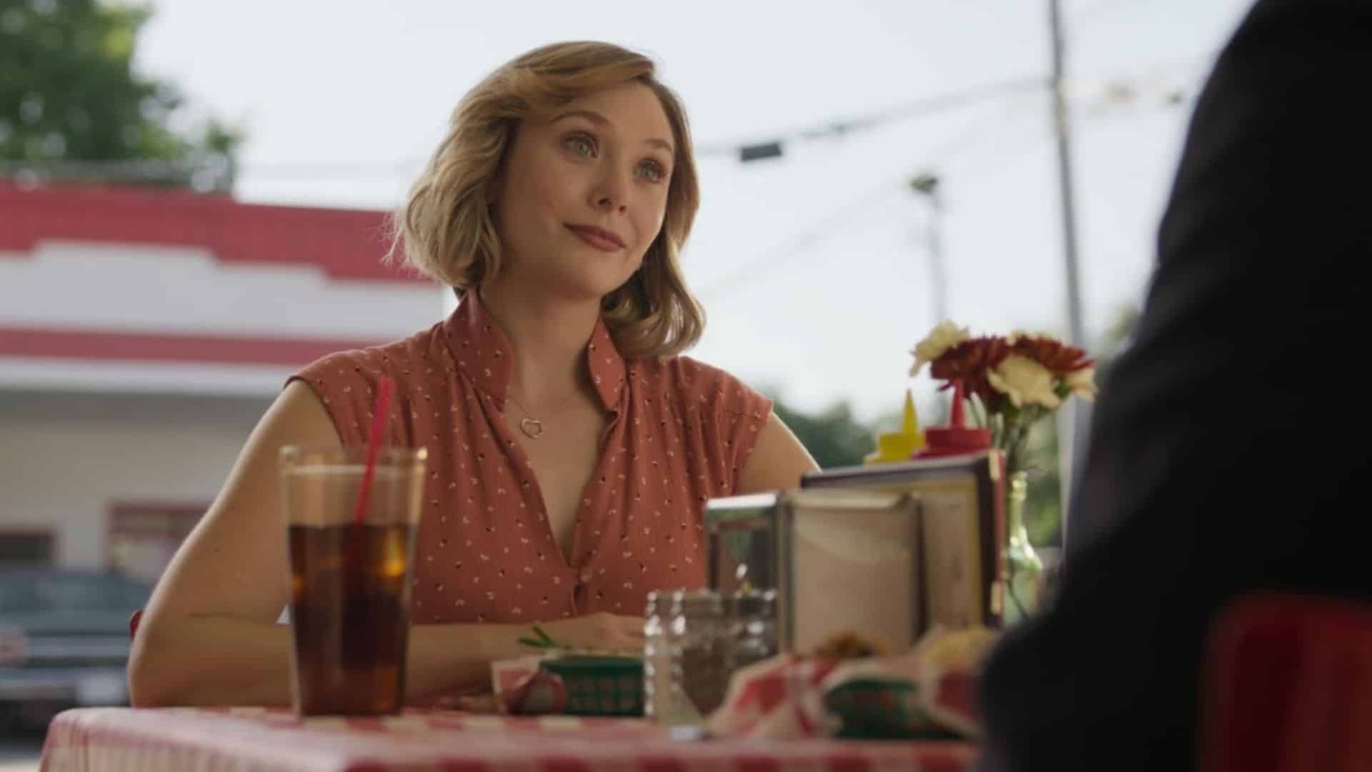 Elizabeth Olsen in a red dress at an outdoor restaurant table in this image from David E. Kelley Productions.