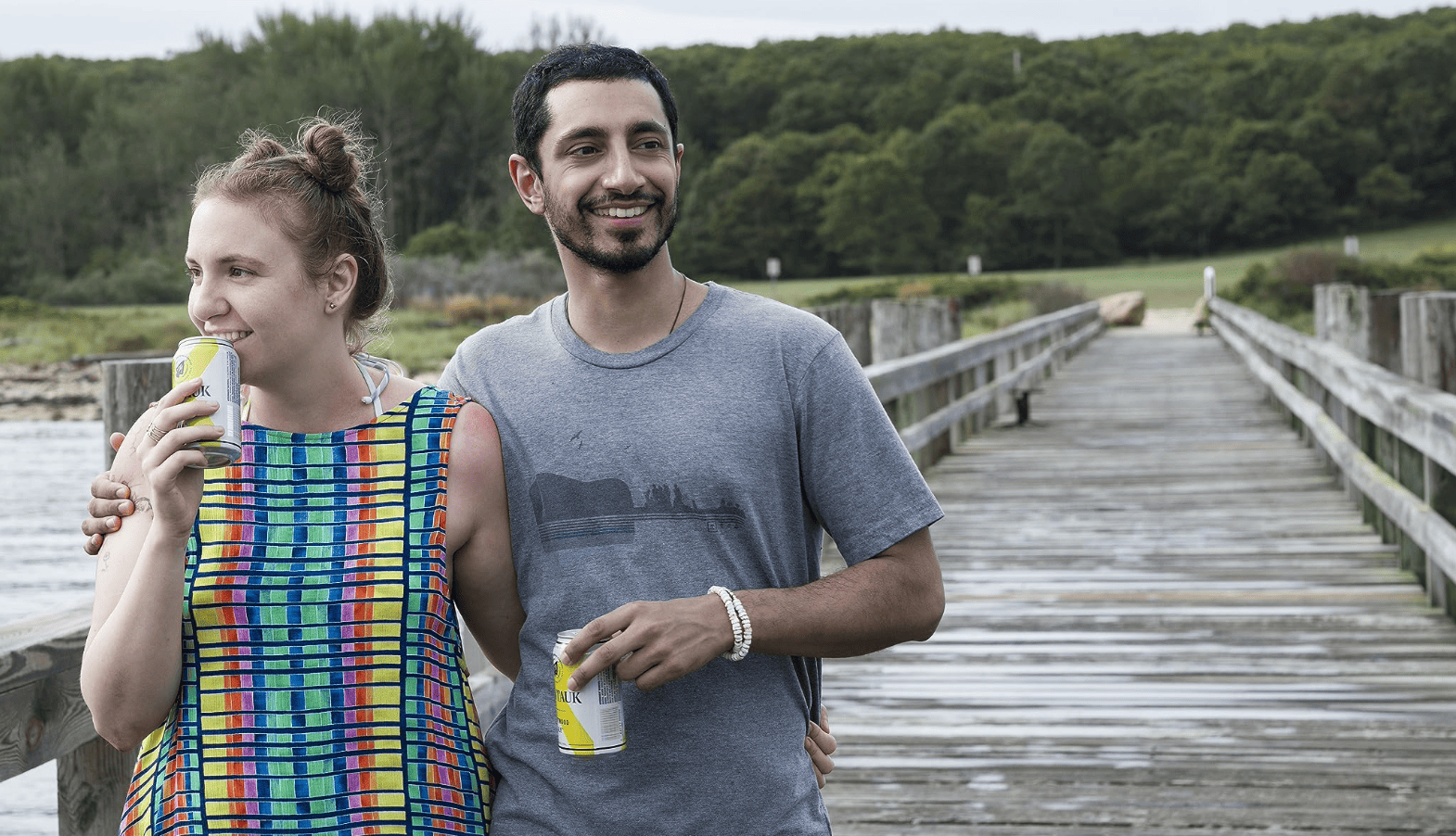 Hannah smiles broadly while walking down a pier embracing Paul-Louis in this image from Apatow Productions.