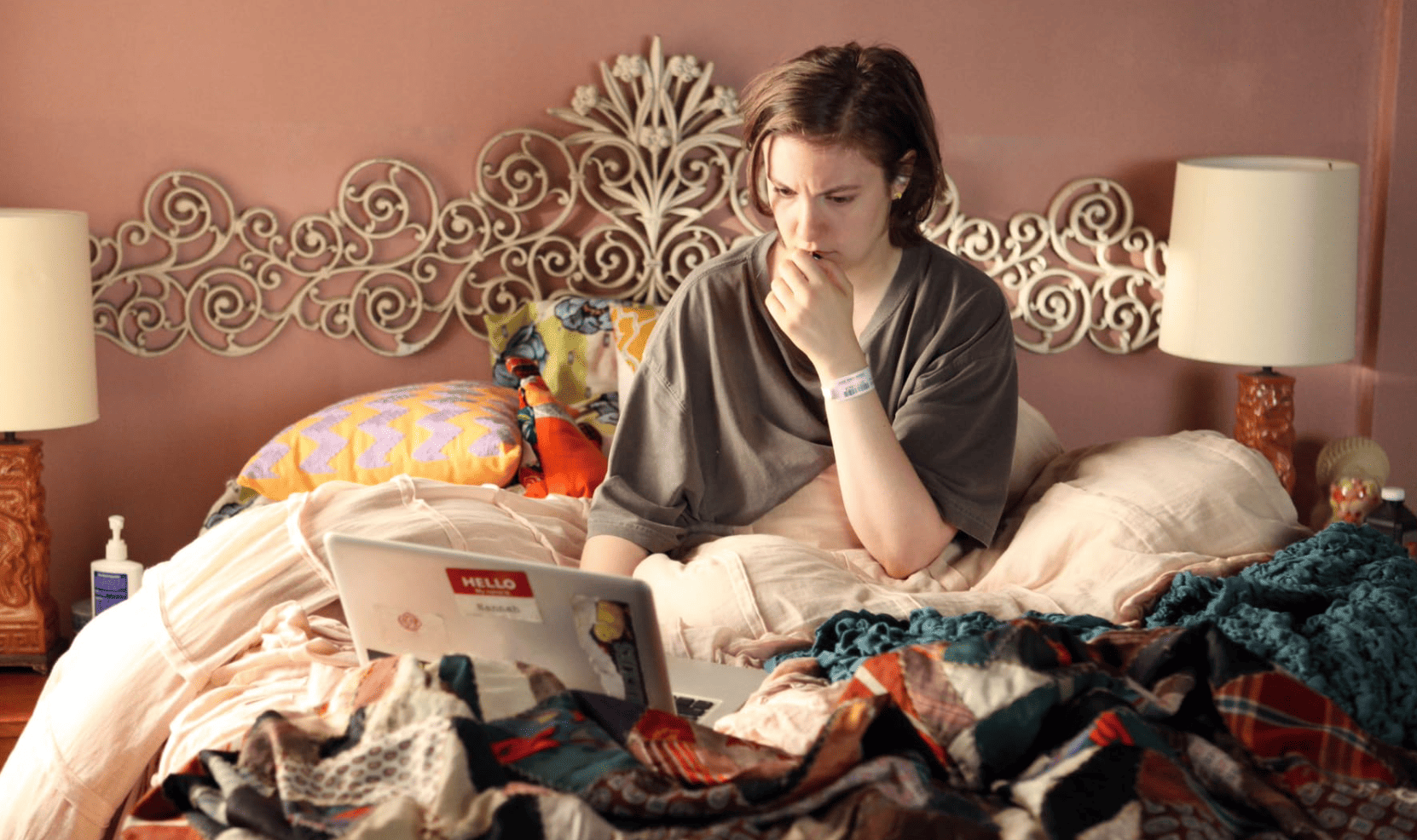 Lena Dunham looking stressed while sitting with her laptop in her messy bed in this image from Apatow Productions