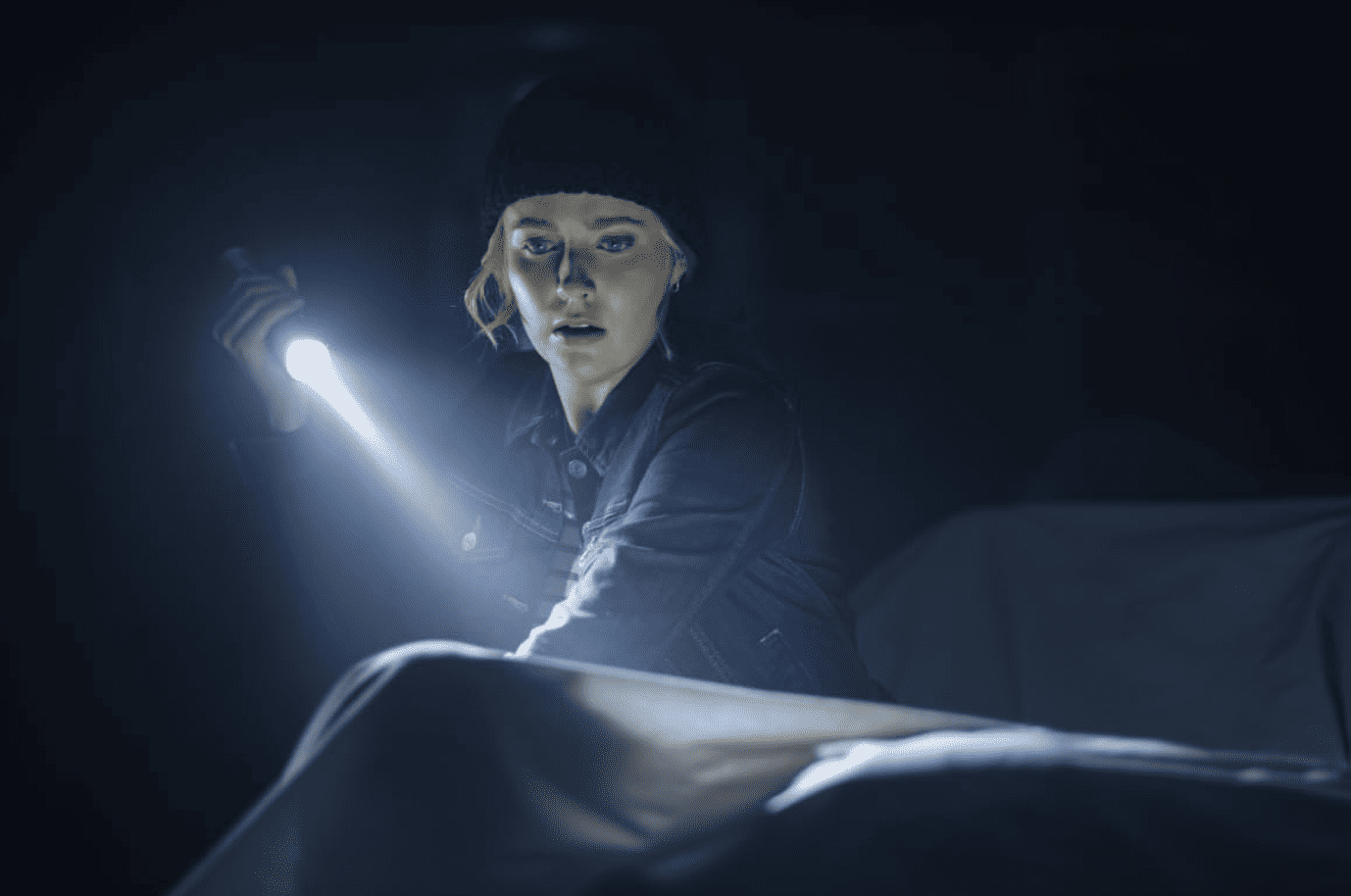 A young woman holds a flashlight in the dark in this image from CBS Television Studios.