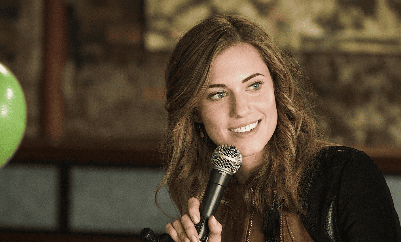 Allison Williams in her role as Marnie holding a microphone mid-conversation in front of an off-camera crowd in this image from Apatow Productions