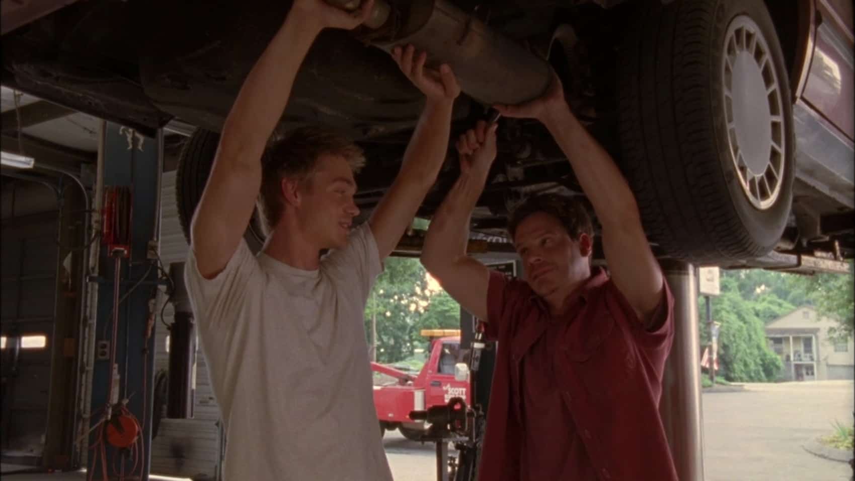 Two men stand under a car in an auto shop in this image from Tollin/Robbins Productions.