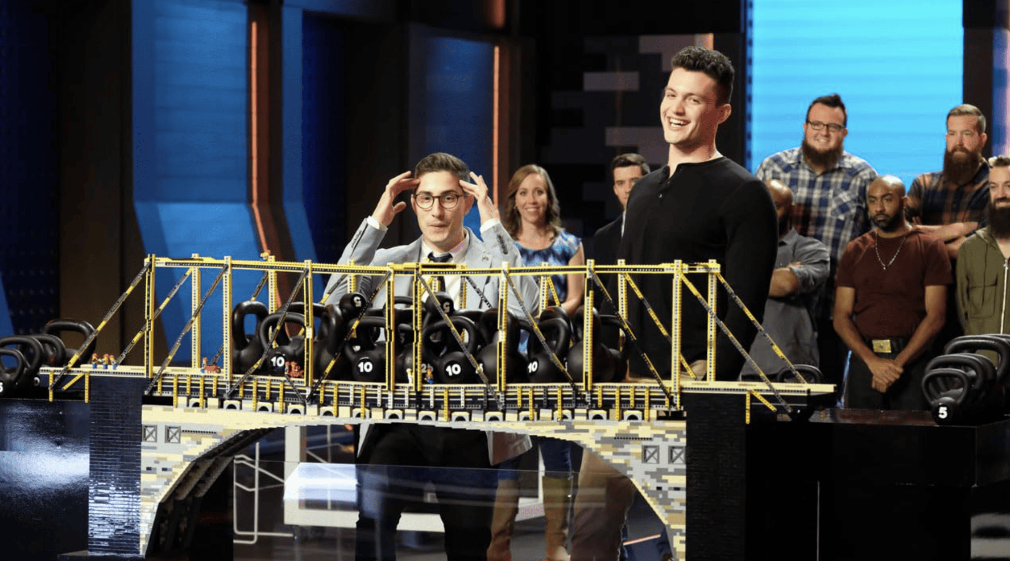 A Lego-built bridge carries the weight of many kettlebells as contestants look on in this image from Endemol Shine North America. 