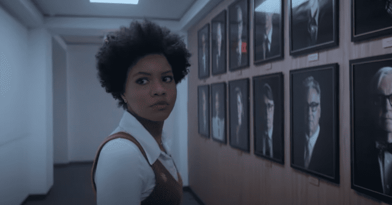  A black woman dressed smartly in a hallway looking away from a wall of portraits in this image from Onyx Collective.