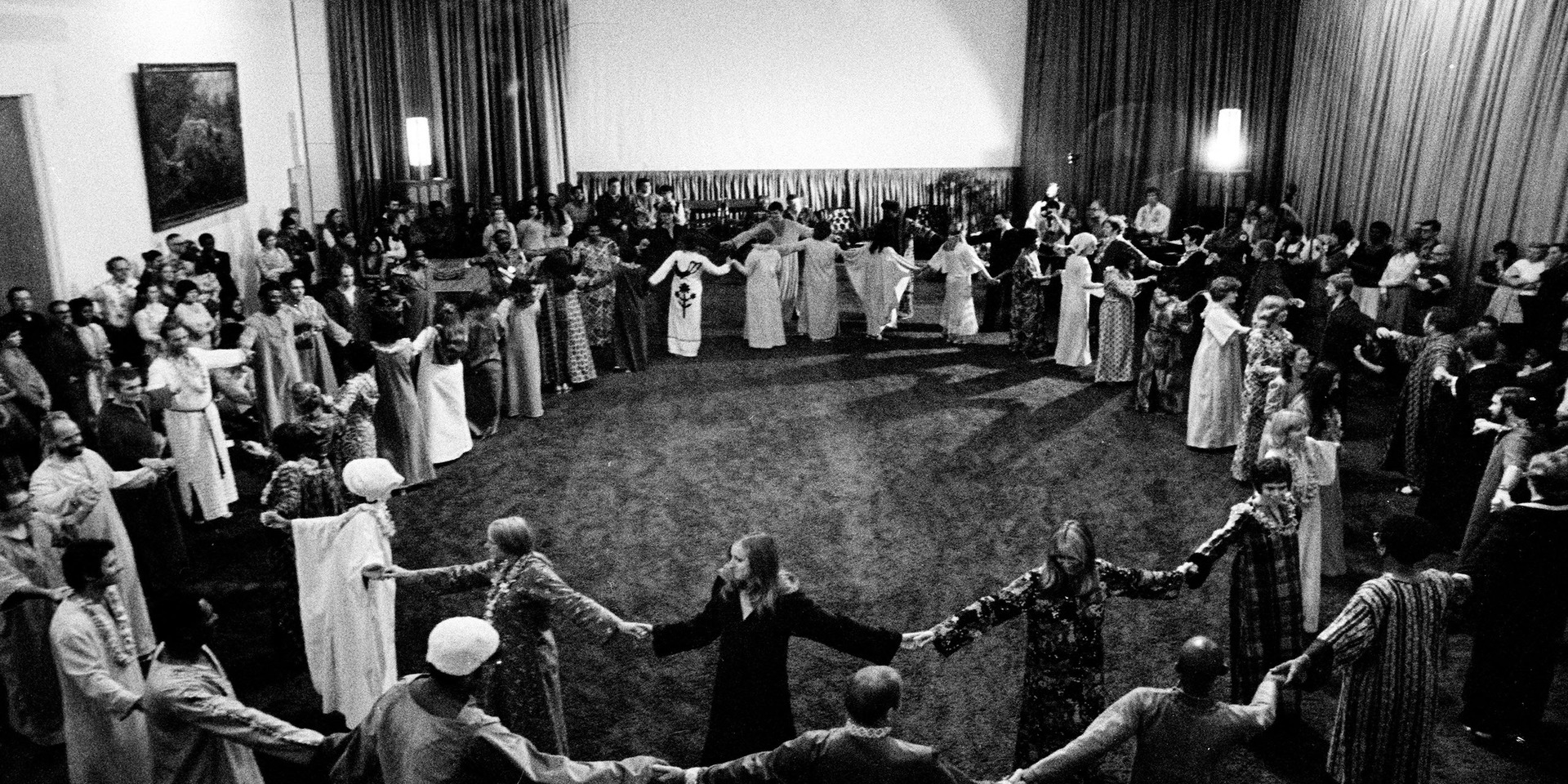 A black and white photo of a cult-like group holding hands in a circle is in this image from HBO Documentary Films.