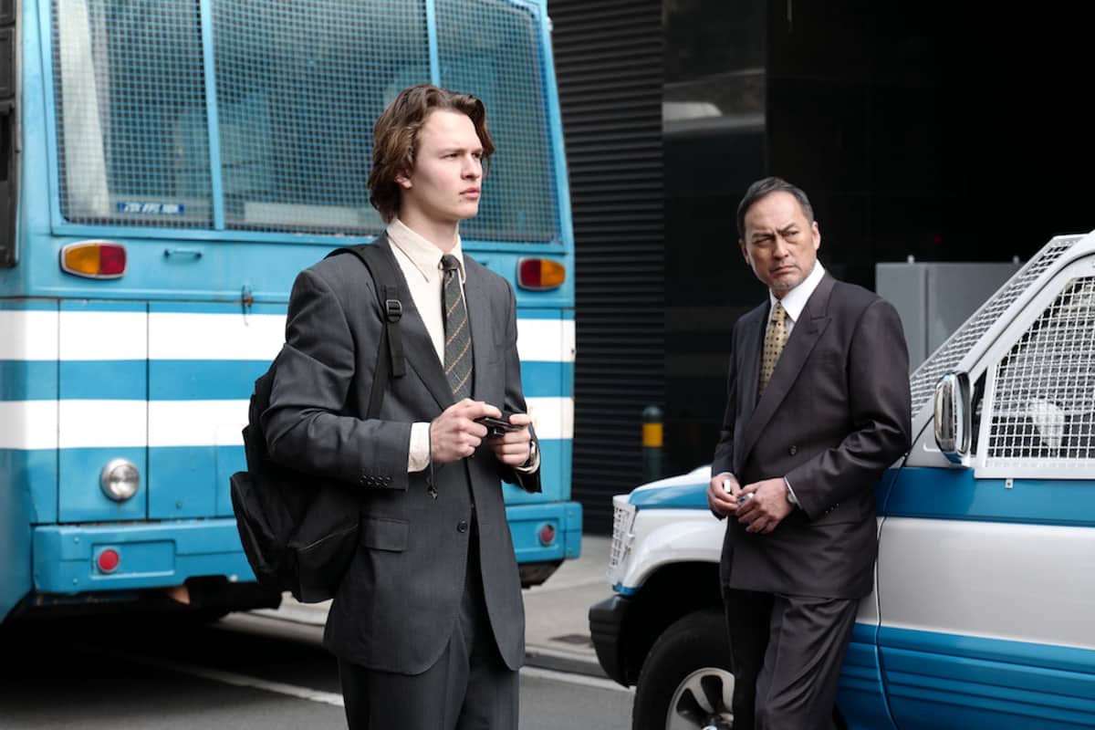 Two suited men stand next to a police car and bus in this image from Boku Films.