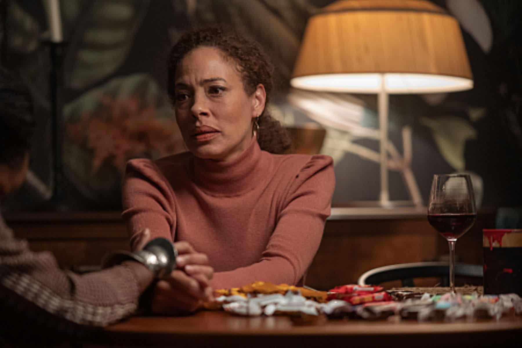 A woman sits at a table and holds hands with another woman slightly out of frame in this photo from Showtime