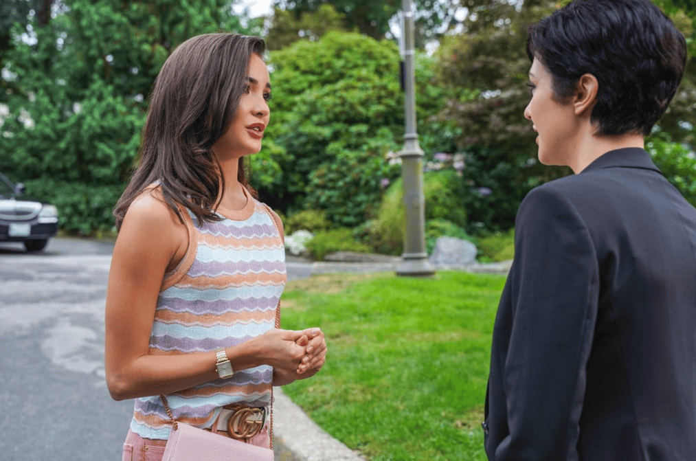 Two women stand in the street talking in this image from CBS Television Studios. 