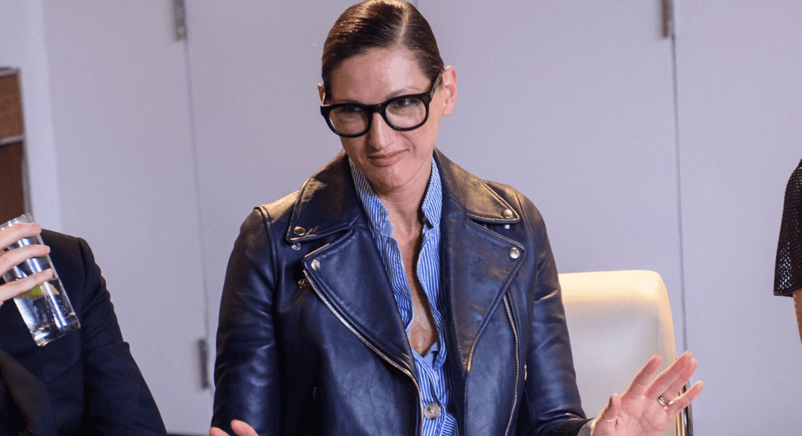 A close-up of Jenna Lyons sitting at a table wearing a leather jacket and big framing glasses in this image from Break Thru Films