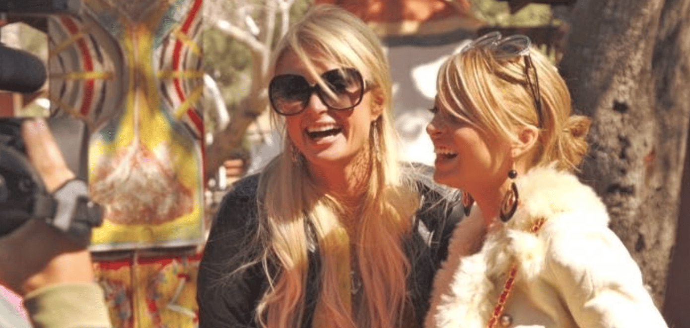 Paris Hilton laughing while wearing her signature sunglasses and standing next to Nicole Richie in this image from 20th Century Fox Television.