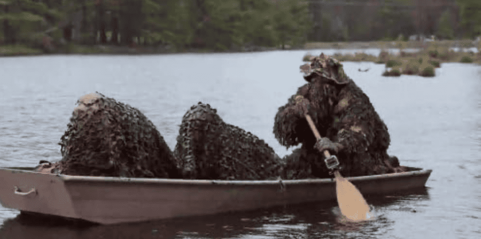 Three individuals rowing a boat down a body of water wearing camouflage suits in this image from Sharp Entertainment.