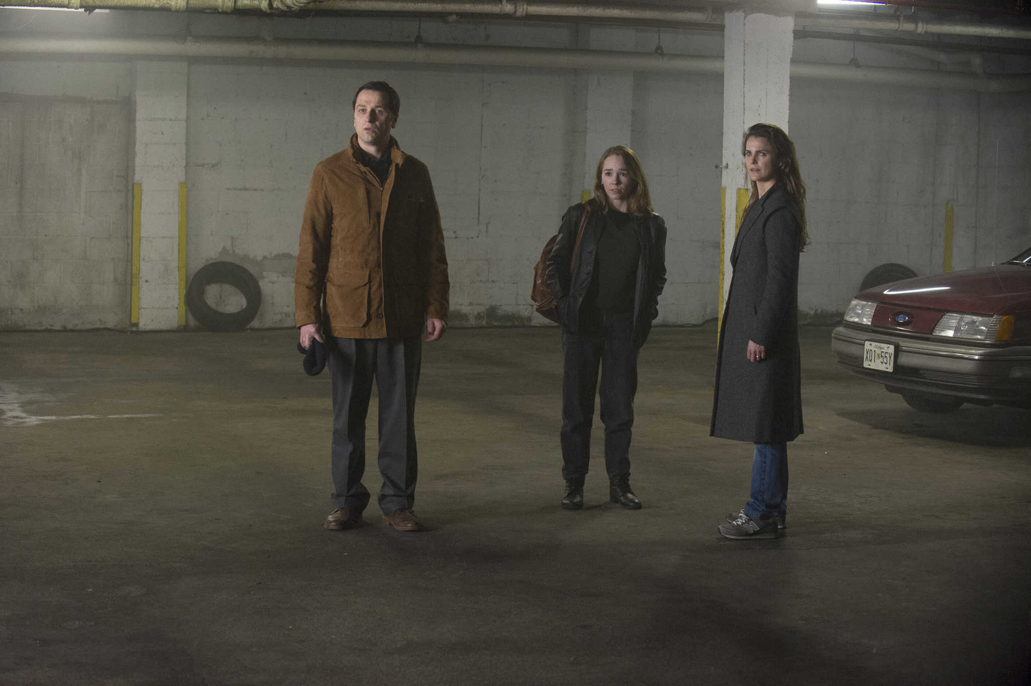 Three people stand around in a parking garage in this image from Amblin Television.