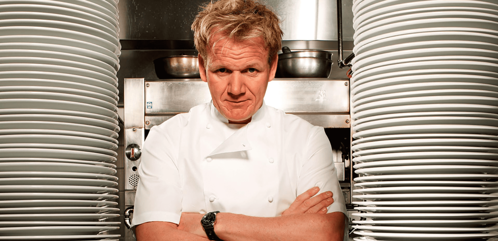 Gordon Ramsay between two stacks of plates while crossing his arms in this image from Studio Ramsay Global.