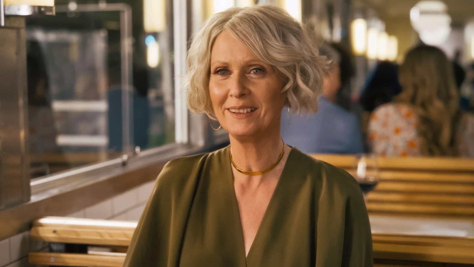 A woman with gray hair sits at a table in a cafe in this image from HBO Entertainment.