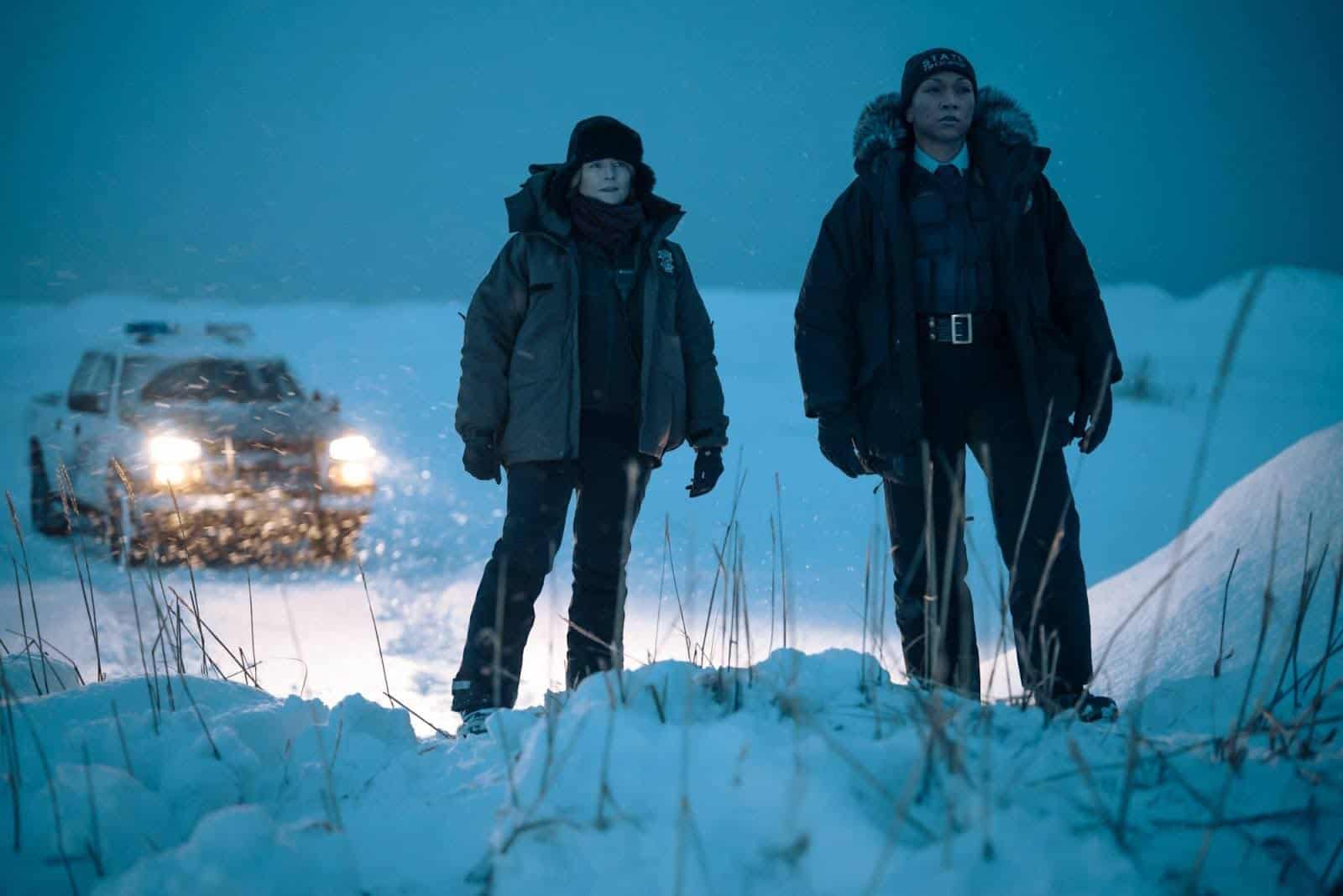 Two police women in parkas search a snowy field in this image from Anonymous Content.
