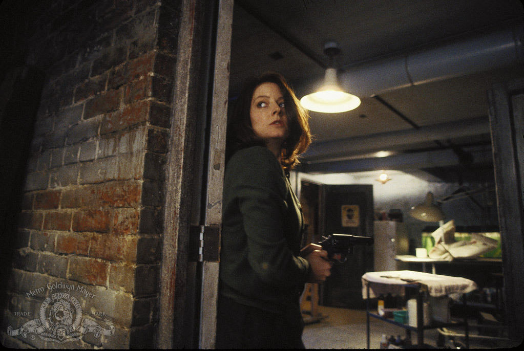 A woman hugs a wall as she holds a gun in this image from Strong Heart Productions.