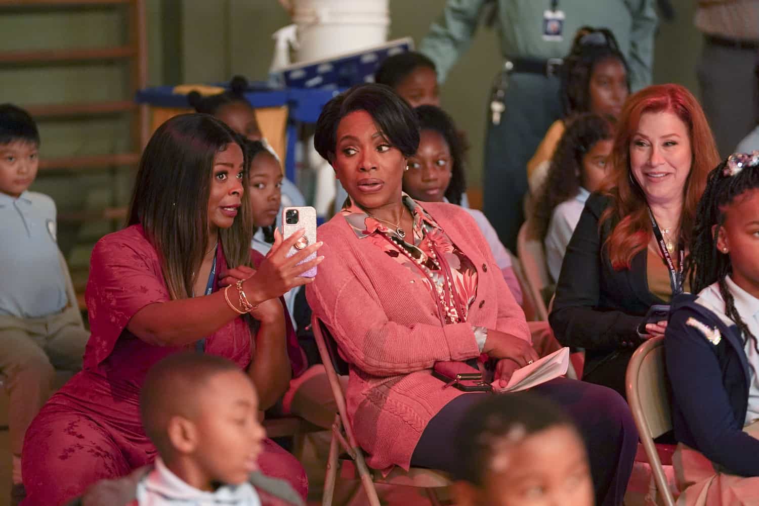 Three women sit in a school assembly in this image from Warner Bros. Television