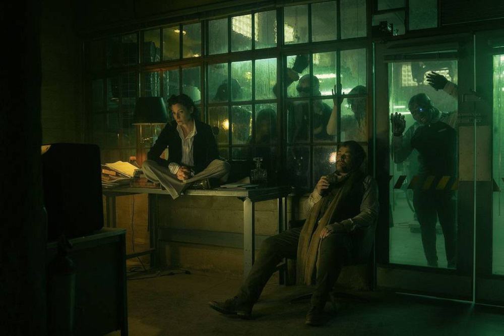 Two people in an office with superheroes clawing at the window in this image from DC Entertainment
