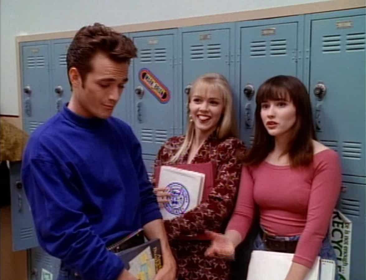 Three high school friends stand together in front of lockers in this photo from Spelling Television.