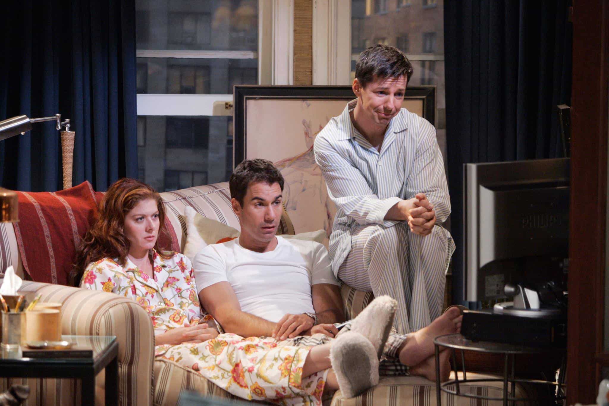 A trio of adult friends are sitting on a couch together in pajamas watching TV in this photo by NBC Studios