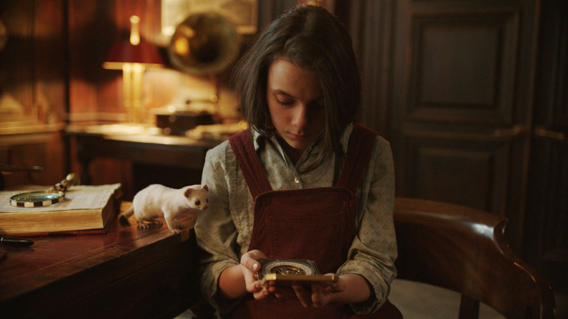 A young girl looks at a strange instrument with a white weasel on the table in this image from New Line Productions.