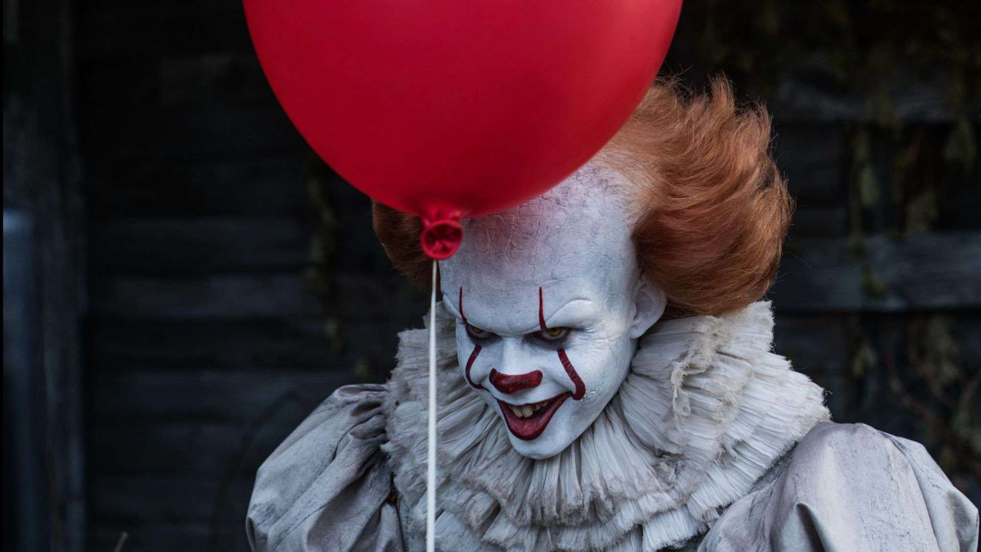 A menacing-looking clown holds a red balloon in this image from New Line Cinema.