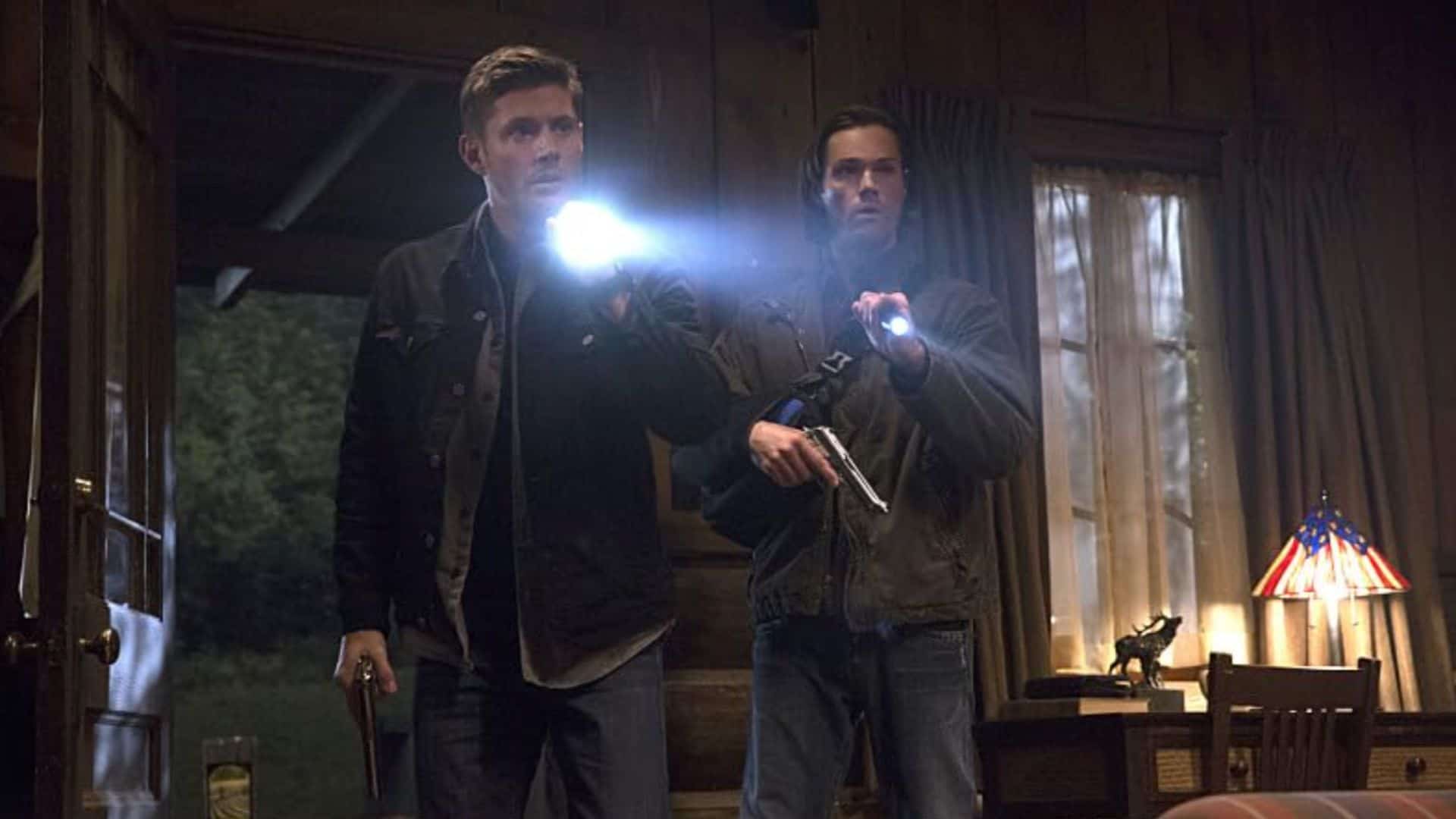 Two men holding guns and flashlights in this image from Warner Bros. Television