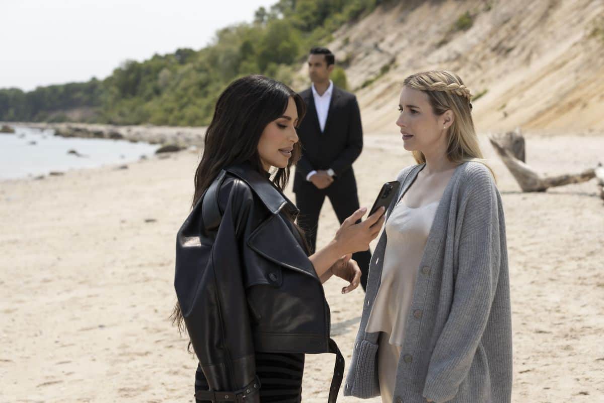 A woman looks at her phone on the beach, standing next to another woman in this image from Ryan Murphy Television.