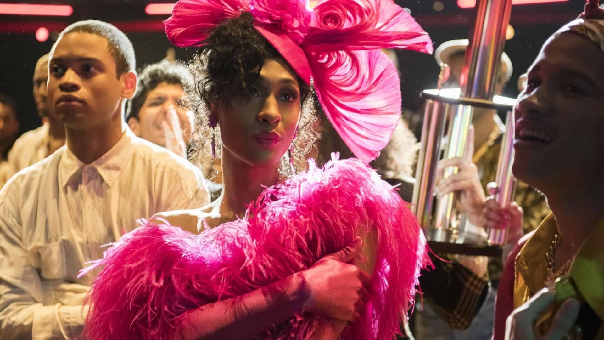 MJ Rodriguez in a pink dress and hat stands in a crowd in this image from FX Productions.