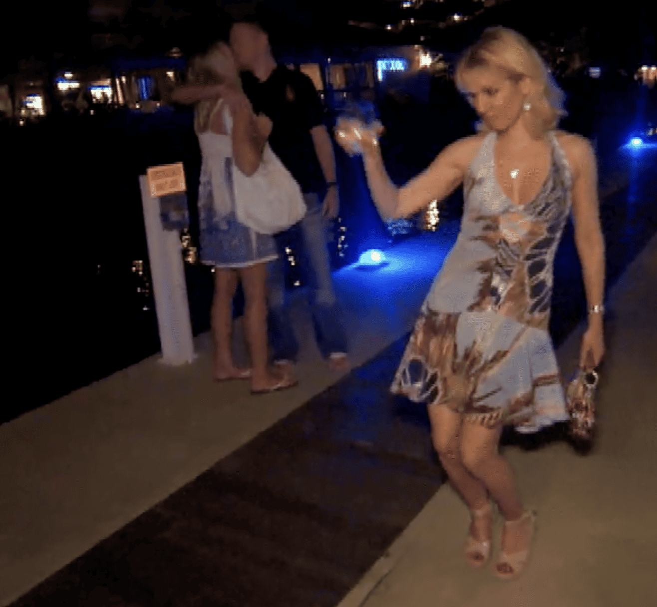  A woman with blond hair holding her purse and a glass of wine dances on the pier in this image from Shed Entertainment.