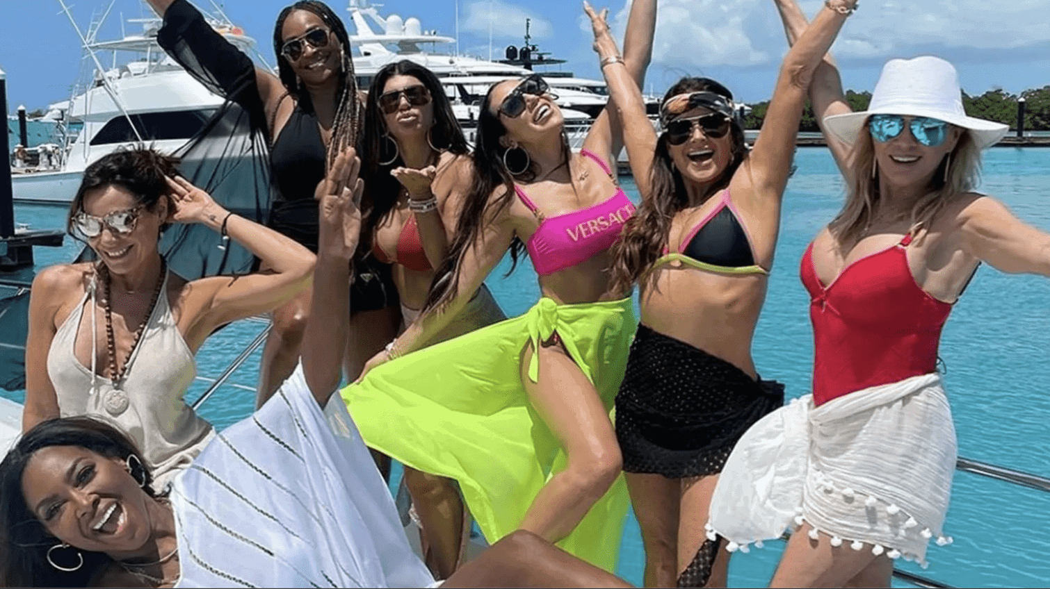 Seven women pose in swimwear and cover-ups and face the camera, raising Champagne flutes in this image from Shed Media.
