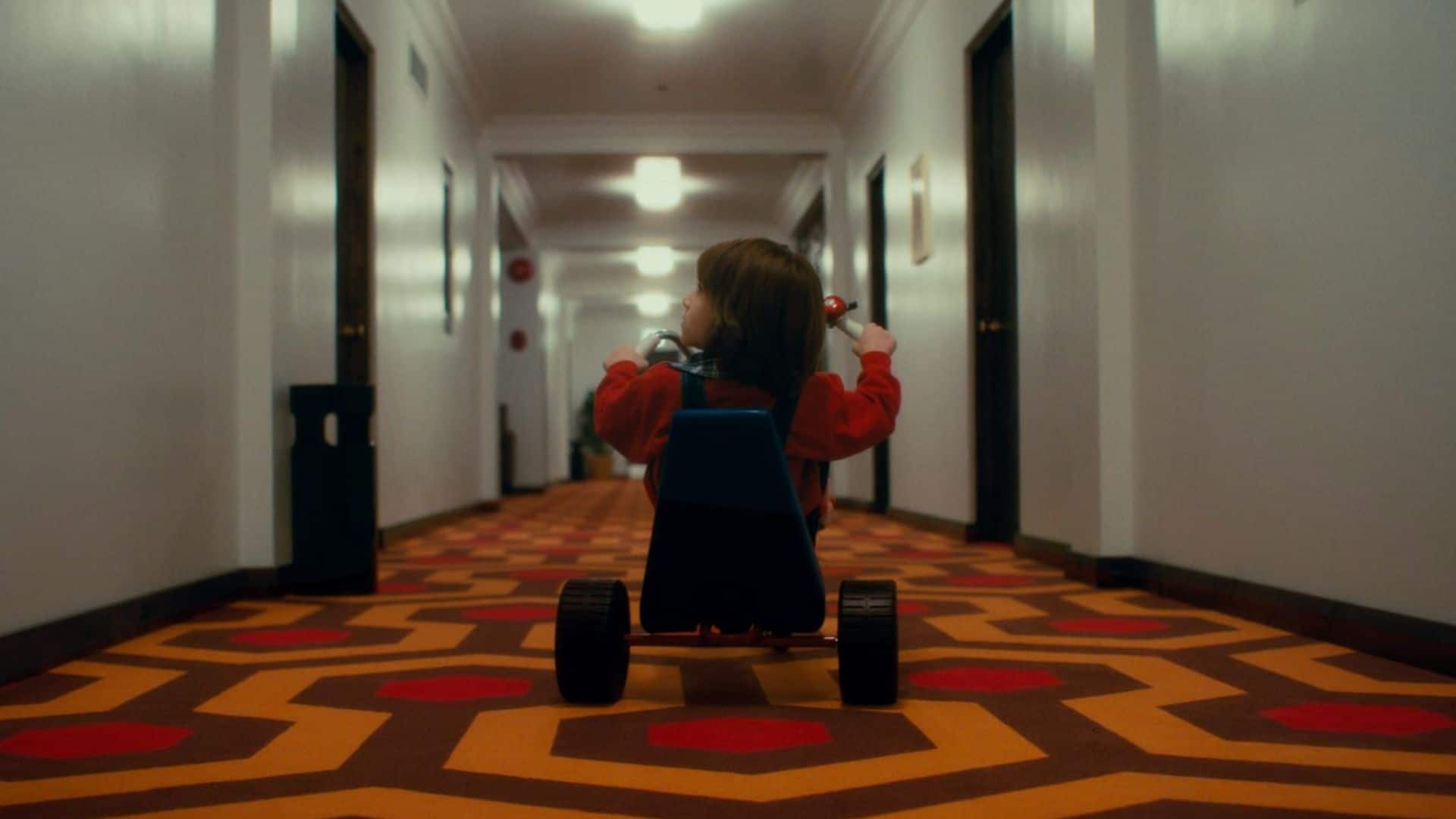 A young boy rides on a tricycle in a hotel hallway in this image from Warner Bros. Pictures.