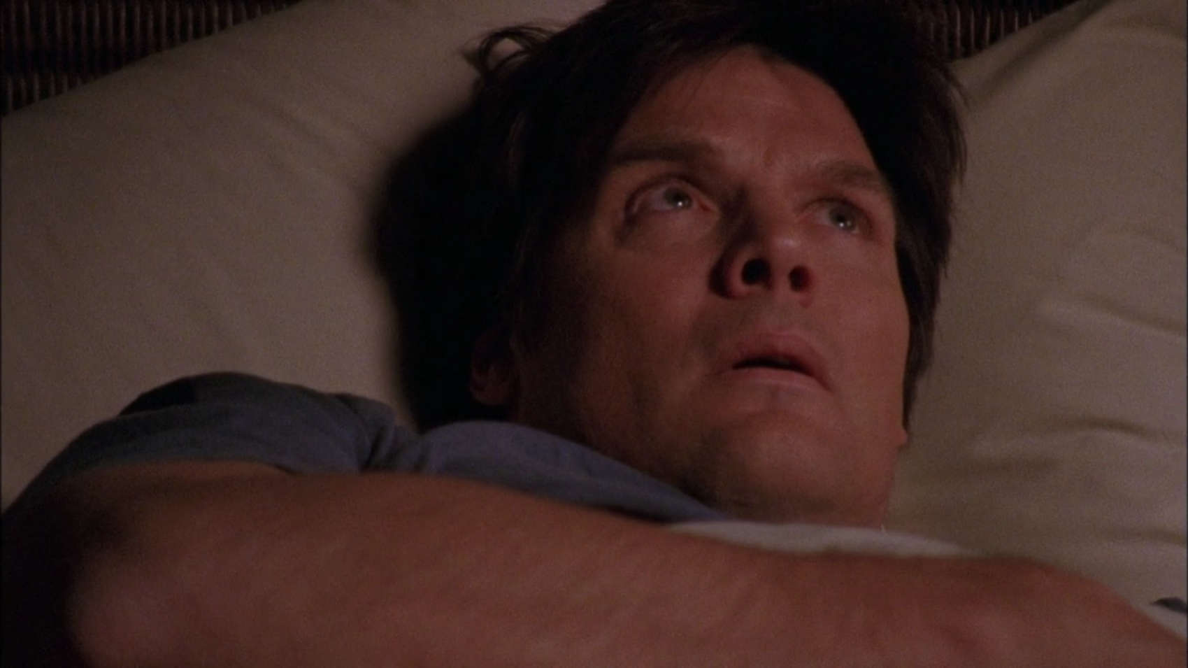 A man lies in bed worriedly staring at the ceiling in this image from Tollin/Robbins Productions.
