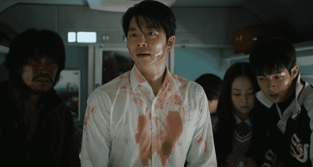 A man wearing a bloodied shirt stands in a train aisle in this image from Next Entertainment World.