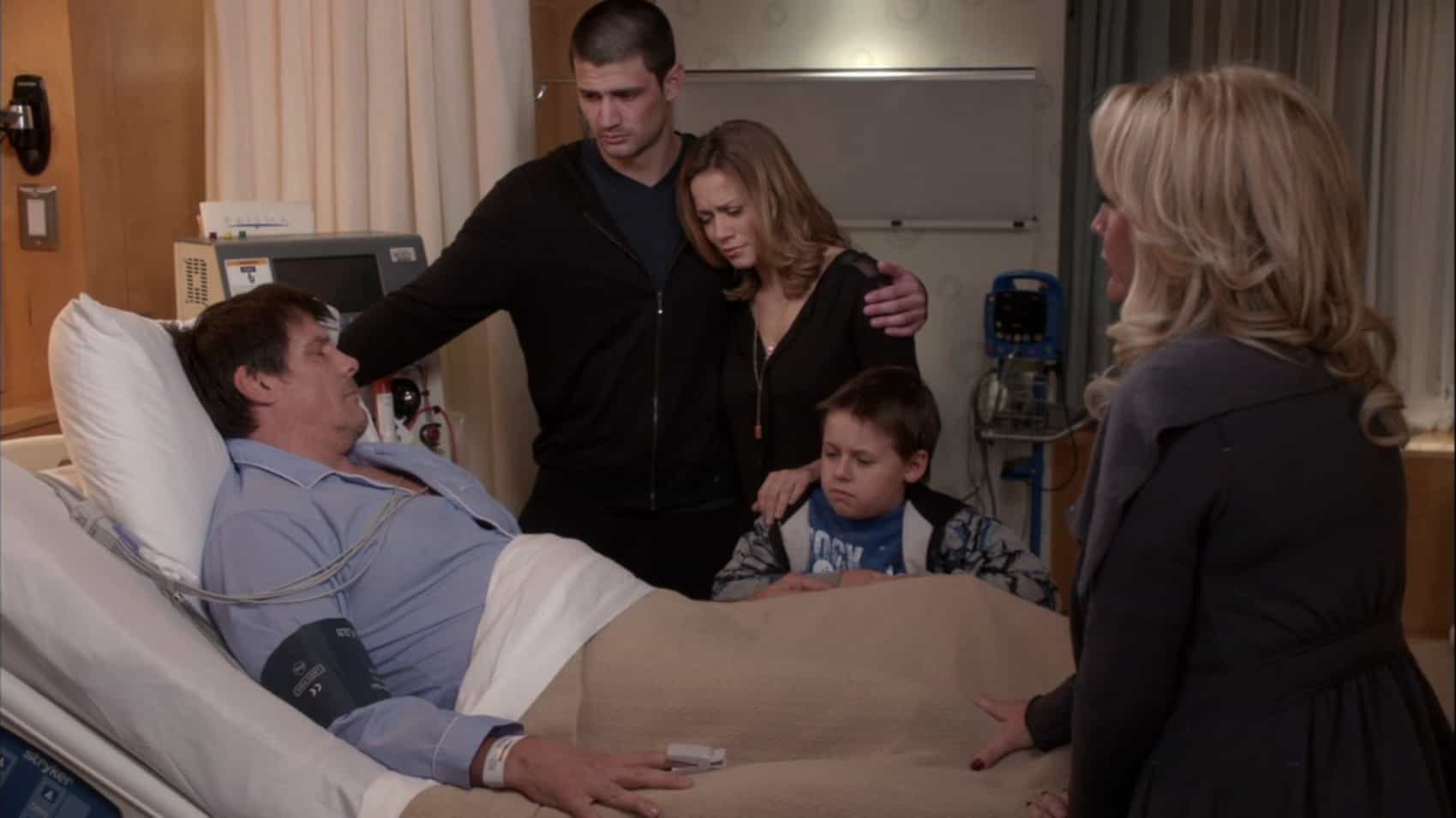 A family stands around a man's deathbed in a hospital in this image from Tollin/Robbins Productions.