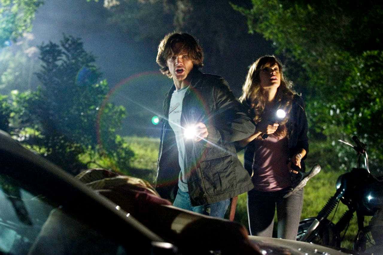 Two young people shine flashlights into a car in the woods in this photo from Paramount Pictures.