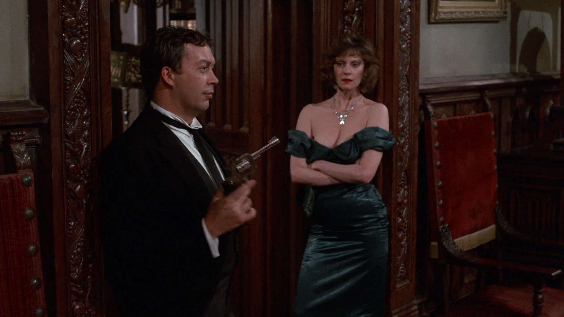 Tim Curry holding a gun while Lesley Ann Warren looks disapproving in this image from The Guber-Peters Company.