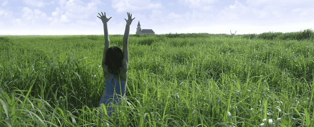 A woman holds up her arms in a field of grass in this image from Copperheart Entertainment.