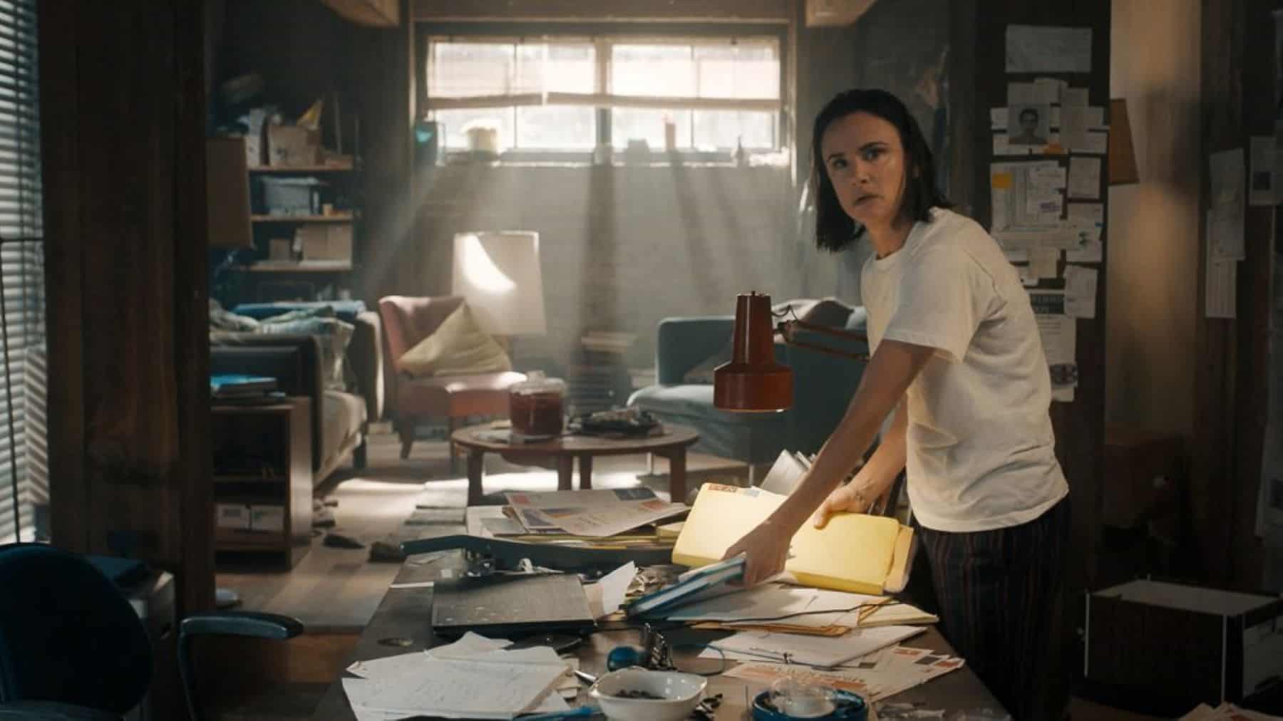 A woman stands next to a messy desk covered in papers and files in this image from Blumhouse Television.